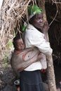 African mother with baby in sling in front of hut, Uganda