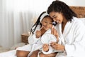 African mother and her little daughter in bathrobes making makeup on bed Royalty Free Stock Photo