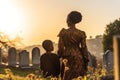 African mother with kid visiting grave in cemetery in sunset at Africa. Generative AI