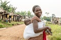 African mother with cute baby in sling in beautiful street of village with straw huts.