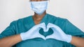 African nurse wear face mask, gloves, blue uniform showing heart hands shape.