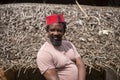 An African Older Man in Red Muslim Taqiyyah Fez Hat posing with a stick for lame people on Yard Near the Basic Hut with