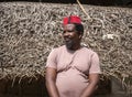 An African Older Man in Red Muslim Taqiyyah Fez Hat posing with a stick for lame people on Yard Near the Basic Hut with