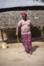 An African Older Man in Red Muslim Taqiyyah Fez Hat posing with a stick for lame people on Yard Near the Basic Hut with