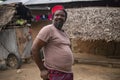 An African Older Man in Red Muslim Taqiyyah Fez Hat posing with a stick for lame people on Yard Near the Basic Hut with