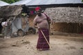 An African Older Man in Red Muslim Taqiyyah Fez Hat posing with a stick for lame people on Yard Near the Basic Hut with