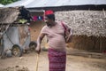 An African Older Man in Red Muslim Taqiyyah Fez Hat posing with a stick for lame people on Yard Near the Basic Hut with