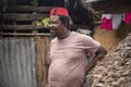 An African Older Man in Red Muslim Taqiyyah Fez Hat posing with a stick for lame people on Yard Near the Basic Hut with