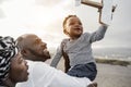 African parents and little son having fun with wood airplane on the beach - Main focus on father face