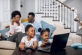 African parents resting on sofa while kids playing on laptop Royalty Free Stock Photo