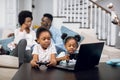 African parents resting on sofa while kids playing on laptop Royalty Free Stock Photo