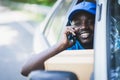 African postal delivery courier man using smart phone and delivering package in car Royalty Free Stock Photo