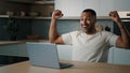 African 30s guy male man sitting at table at kitchen searching in laptop playing game online win feeling winner enjoy Royalty Free Stock Photo