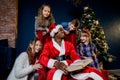 African Santa Claus reads children`s Christmas stories in a cozy decorated New Year`s room.