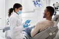 African Stomatologist Woman Discussing Teeth Treatment Process With Male Patient In Clinic