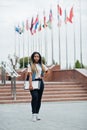 African student female posed with backpack and school items on yard of university, against flags of different countries