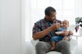 African toddler baby girl crying and don`t want to eat food from her father who feeding with spoon while sitting on sofa at home. Royalty Free Stock Photo