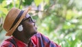 African traveler man sits happily listening to music on his mobile phone in the middle of nature with hat and sunglasses Royalty Free Stock Photo