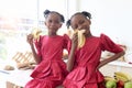 African twin girl sister with curly hair braid African hairstyle eating banana in kitchen. Happy smiling kid sibling eating fruit Royalty Free Stock Photo