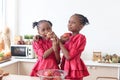 African twin girl sister with curly hair braid African hairstyle eating red apples in kitchen. Happy smiling kid sibling eating Royalty Free Stock Photo