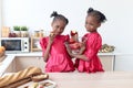 African twin girl sister with curly hair braid African hairstyle eating red apples in kitchen. Happy smiling kid sibling eating Royalty Free Stock Photo