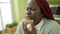 African woman with braided hair eating cookie with closed eyes at dinning room
