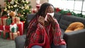 African woman feeling sick sitting on the sofa by christmas tree at home