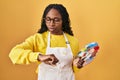 African woman holding painter palette checking the time on wrist watch, relaxed and confident Royalty Free Stock Photo