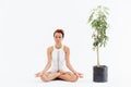 African woman meditating in lotus pose near tree in pot