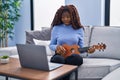 African woman playing ukulele at home doing video call scared and amazed with open mouth for surprise, disbelief face