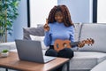 African woman playing ukulele at home doing video call smiling with an idea or question pointing finger with happy face, number