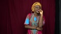 A cheerful black woman in African traditional clothes clasps her hand to her lips, her hands in scars