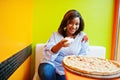 African woman pours salt to pizza while sitting at bright colored restaurant Royalty Free Stock Photo