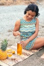 African Woman sitting on the beach uncorking a bottle of wine