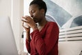 African woman sitting in bed sipping on coffee looking at laptop Royalty Free Stock Photo