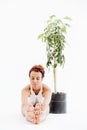 African woman sitting near tree in pot and doing yoga