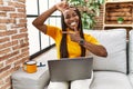 African woman sitting on the sofa using laptop at home smiling making frame with hands and fingers with happy face Royalty Free Stock Photo