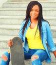 African woman with skateboard sitting in city