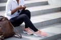 African woman using smart phone while sitting on white stairs outdoors. Royalty Free Stock Photo