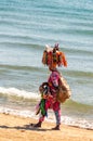 The african woman walking on the beach while holding on her head and the hands various bijouterie, frippery, ornamentals to buy