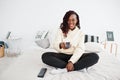African woman watching tv at home and holding a remote control on bed Royalty Free Stock Photo
