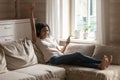 African woman wearing headphones resting on couch singing favourite song