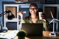 African woman working using computer laptop at night with a big smile on face, pointing with hand finger to the side looking at Royalty Free Stock Photo