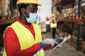 African worker man using tablet inside warehouse while wearing safety mask - Focus on face