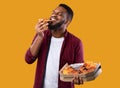 African Young Man Enjoying Pizza Posing With Box, Yellow Background