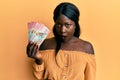African young woman holding 100 new zealand dollars banknote scared and amazed with open mouth for surprise, disbelief face Royalty Free Stock Photo
