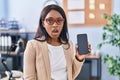 African young woman holding smartphone showing blank screen scared and amazed with open mouth for surprise, disbelief face Royalty Free Stock Photo