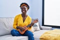 African young woman playing ukulele at home smiling with a happy and cool smile on face