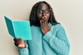 African young woman reading a book wearing glasses covering mouth with hand, shocked and afraid for mistake Royalty Free Stock Photo
