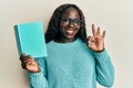 African young woman reading a book wearing glasses doing ok sign with fingers, smiling friendly gesturing excellent symbol Royalty Free Stock Photo